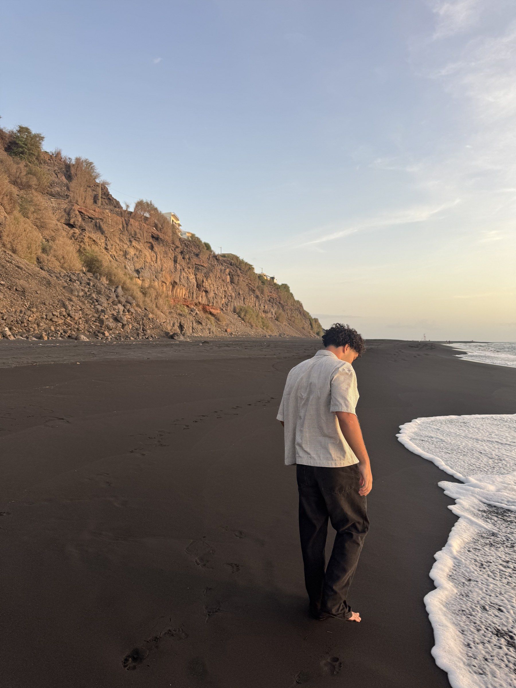 Orhun walking along a black sand beach at sunset