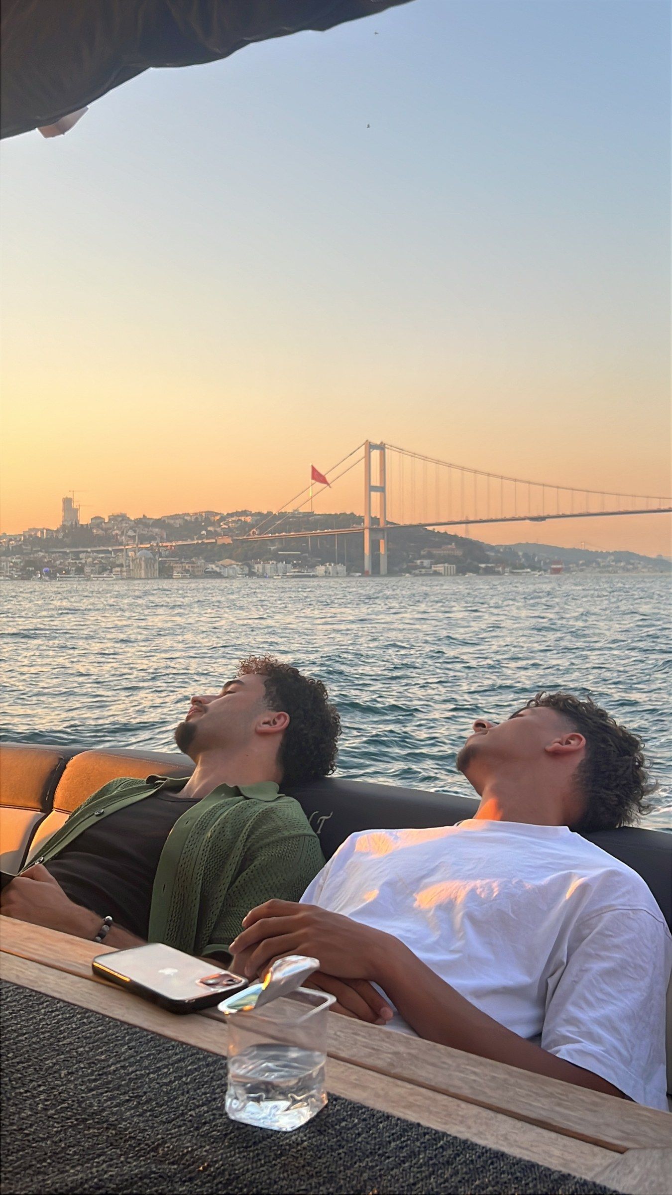 Two guys leaning back on a boat on the Bosphorus at sunset, the bridge behind them