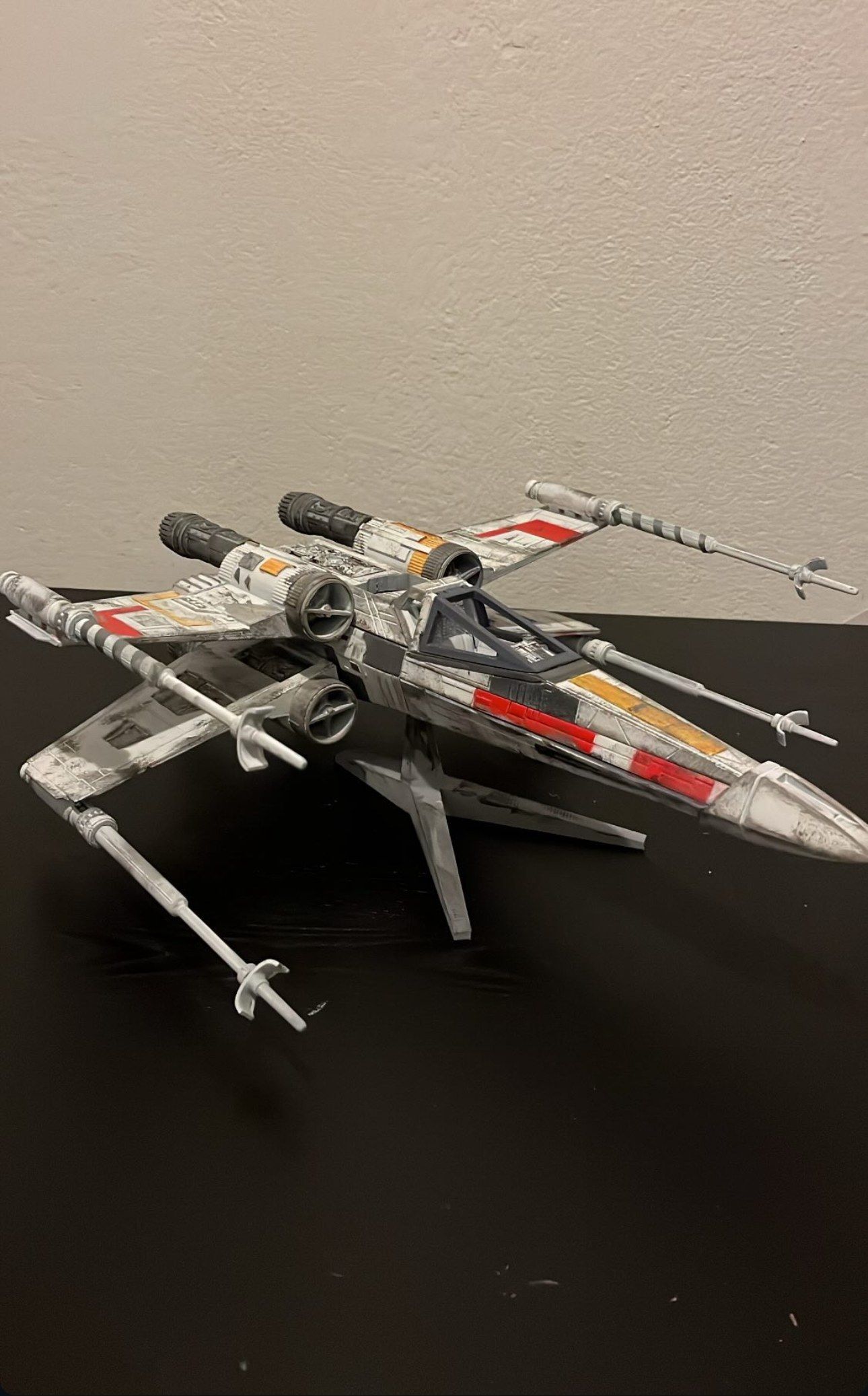 The finished, weathered X-wing model standing on a dark table against a light wall