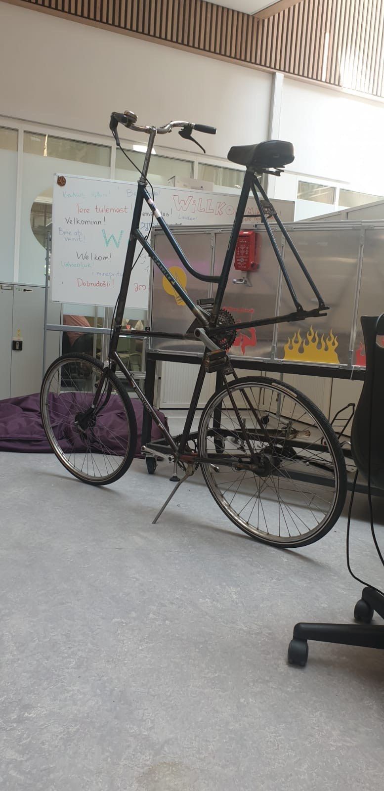 A finished tallbike, two black bike frames welded on top of each other, standing in a university hallway