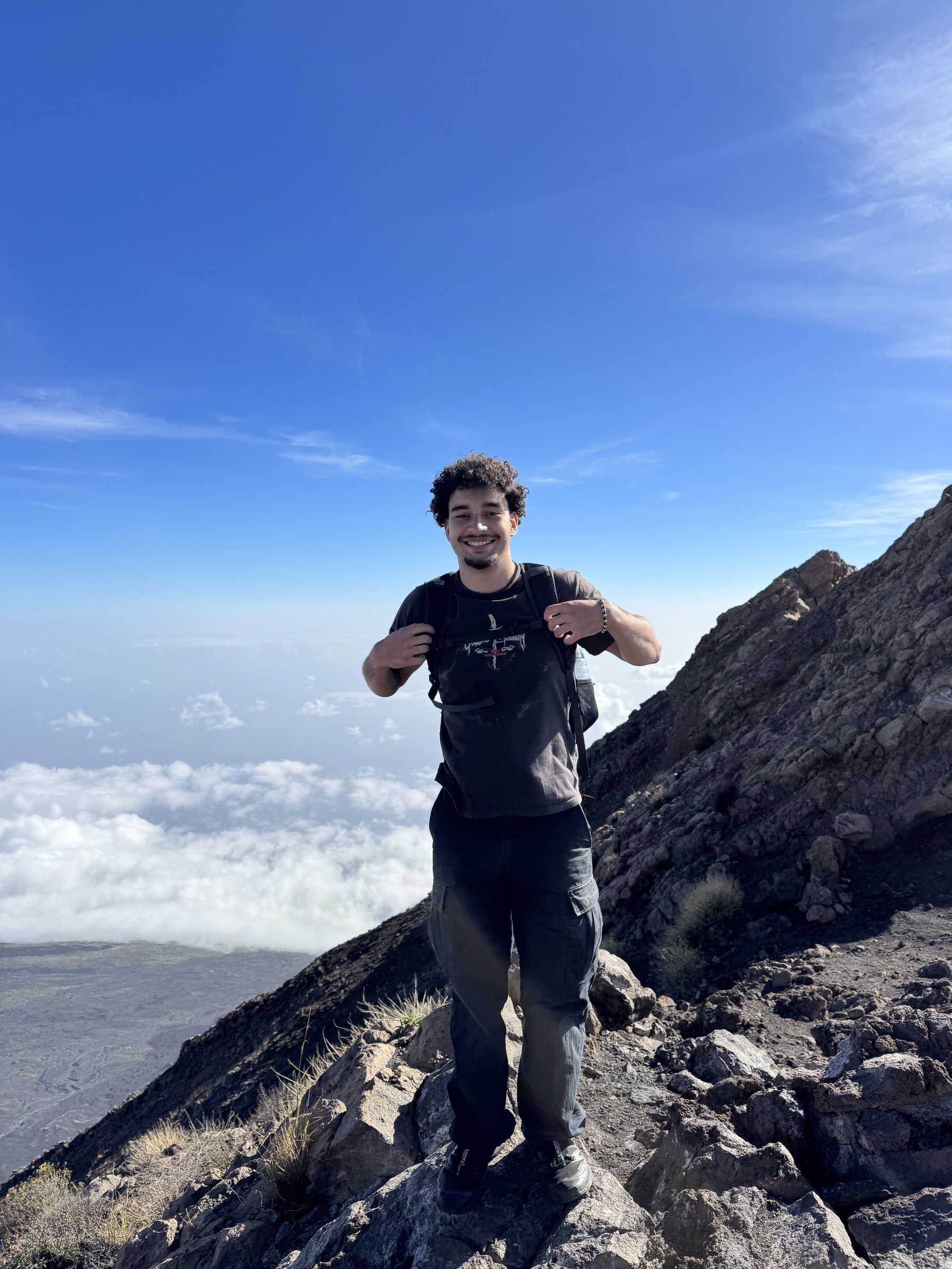 Orhun on the steep rocky rim of Pico do Fogo above the clouds