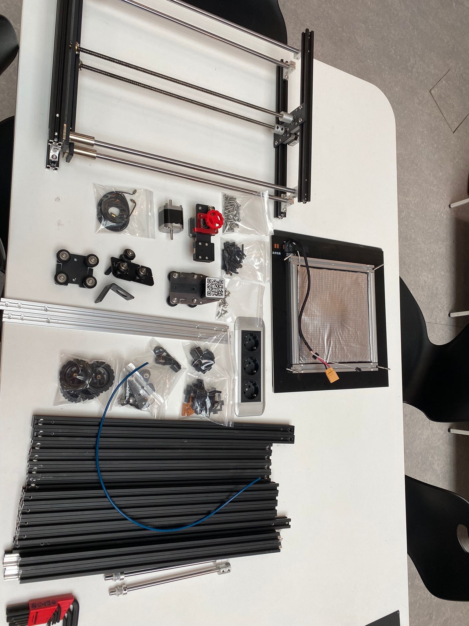 All printer parts laid out on a table: extrusions, rods, motors, brackets and a display