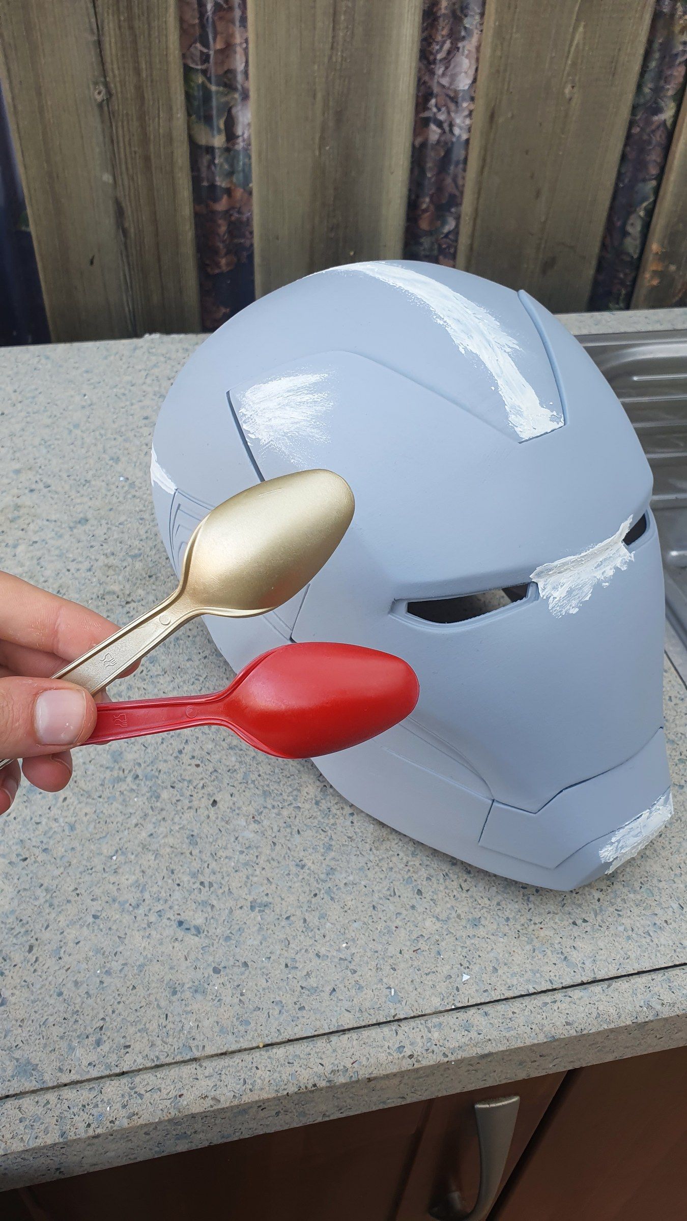 The helmet in grey primer next to a pair of spoons for scale