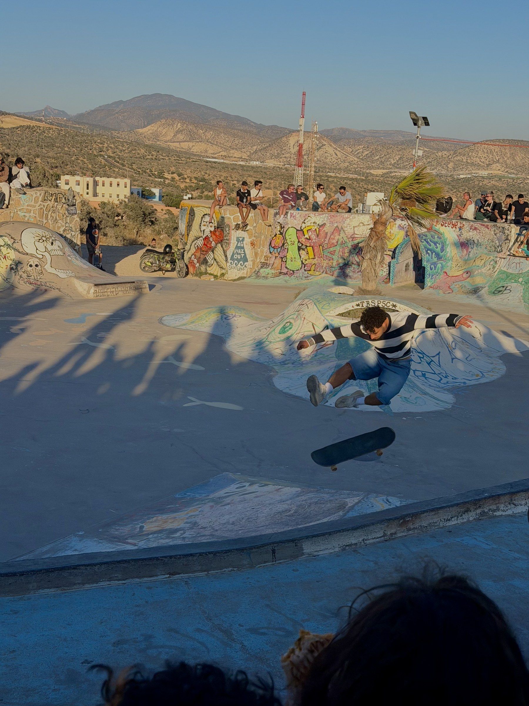Orhun in the air above the bowl, the skateboard flipping below him