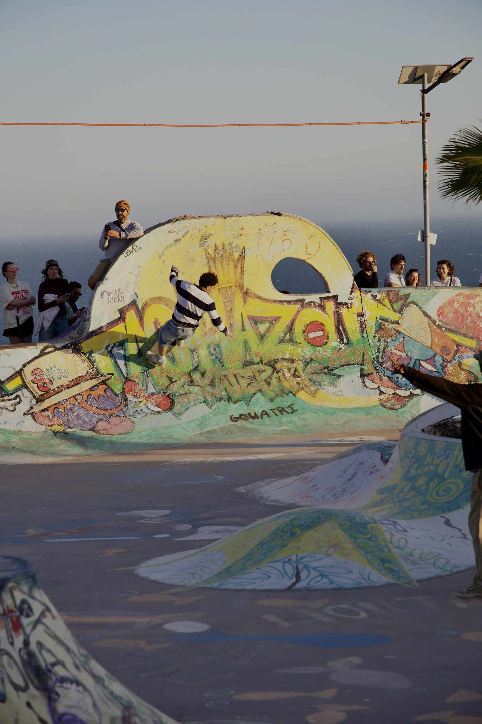 Orhun dropping into a graffiti-covered concrete bowl by the sea while a crowd watches from the lip