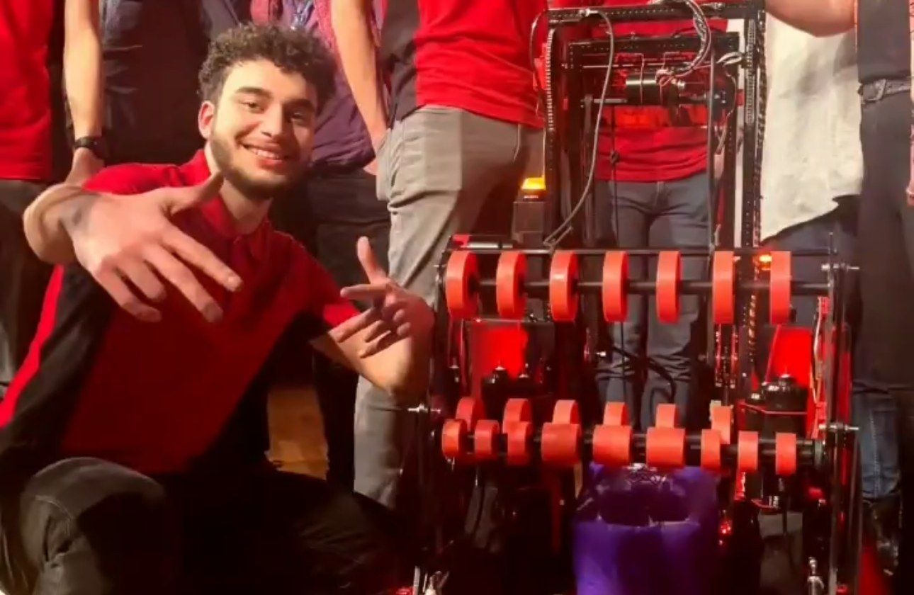 Orhun crouching next to the red Team Pi robot on stage