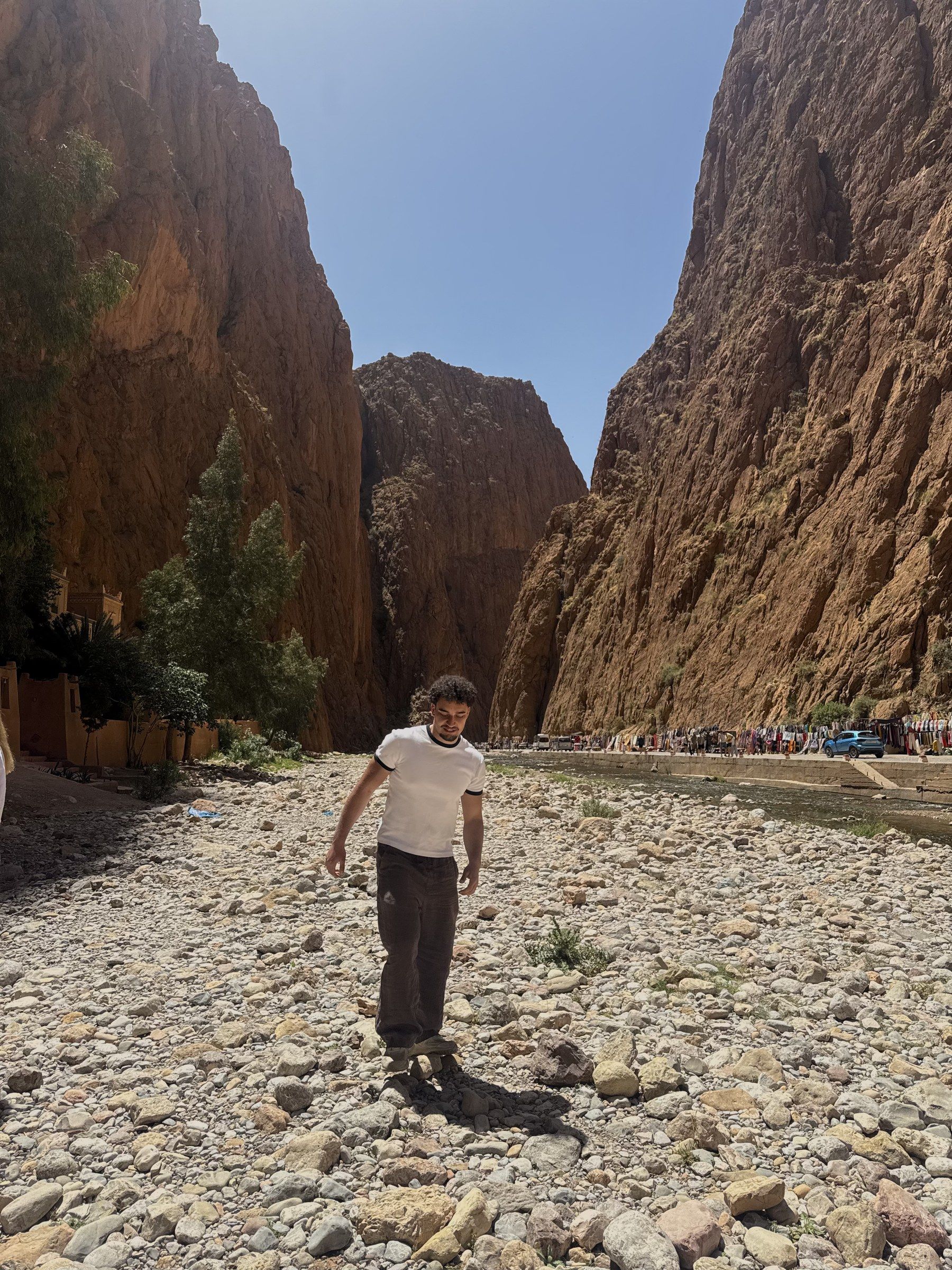 Orhun walking through the dry riverbed of the Todra Gorge between huge red cliffs